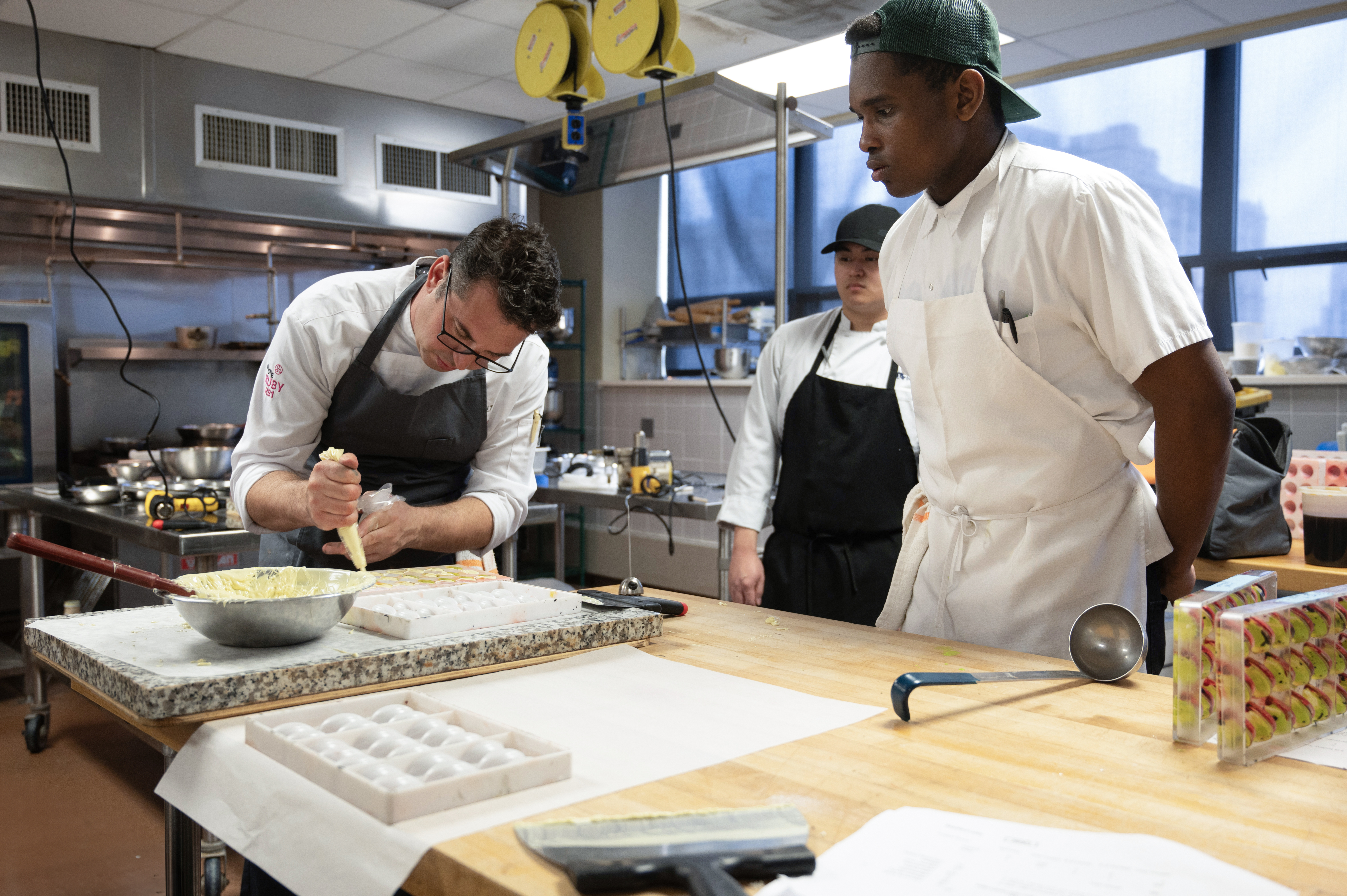 two students observe as faculty member pipes chocolate
